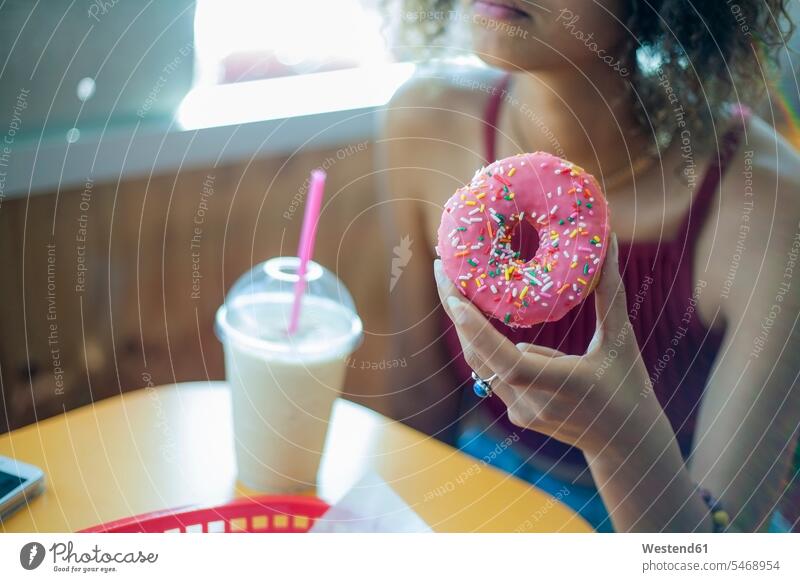 Junge Frau isst Doughnut, während sie im Café sitzt Farbaufnahme Farbe Farbfoto Farbphoto Tag Tageslichtaufnahme Tageslichtaufnahmen Tagesaufnahme am Tag