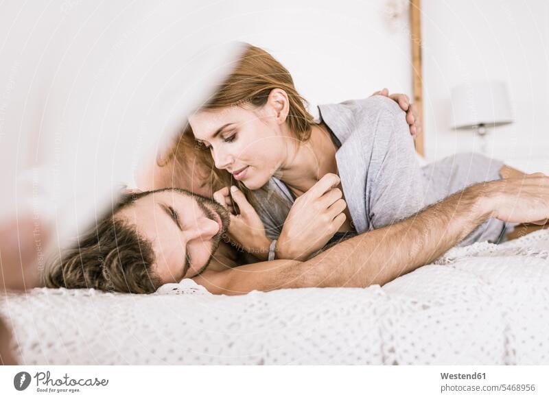 Liebevolles junges Paar im Bett liegend Betten entspannen relaxen knuddeln schmusen Arm umlegen Umarmung Umarmungen entspanntheit relaxt geniessen Genuss intim