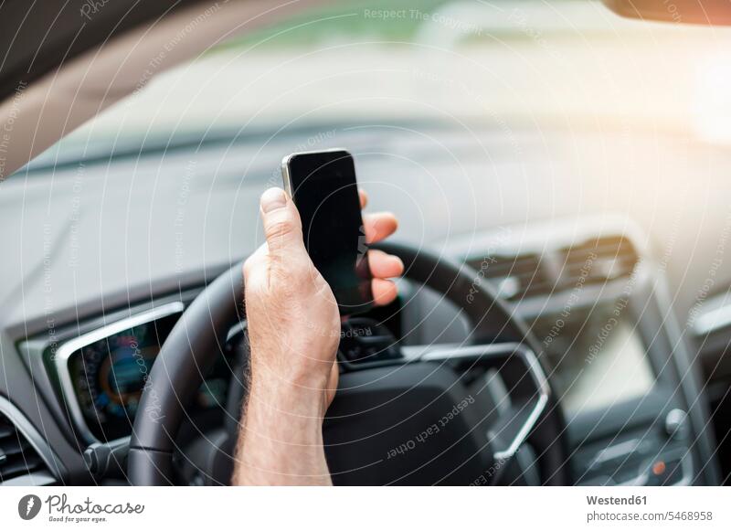 Abgetrennte Hand eines Mannes, der im Auto ein Smartphone über das Lenkrad hält Farbaufnahme Farbe Farbfoto Farbphoto Deutschland Außenaufnahme außen draußen