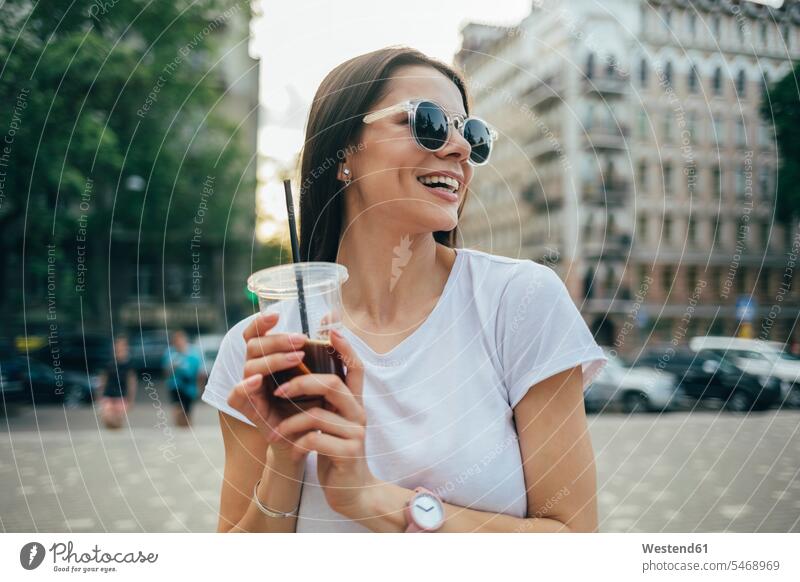 Fröhliche schöne Frau mit Sonnenbrille, die in der Stadt stehend ein Erfrischungsgetränk in der Hand hält Farbaufnahme Farbe Farbfoto Farbphoto Ukraine