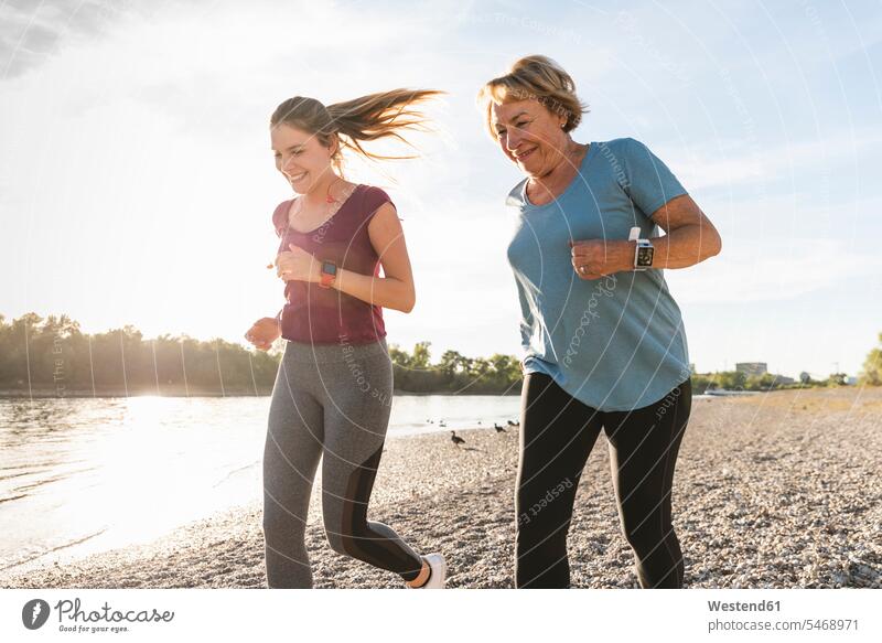 Enkelin und Großmutter haben Spaß, joggen zusammen am Fluss Grossmutter Oma Grossmama Großmütter Omi Enkeltochter Enkelinnen Enkeltöchter laufen rennen