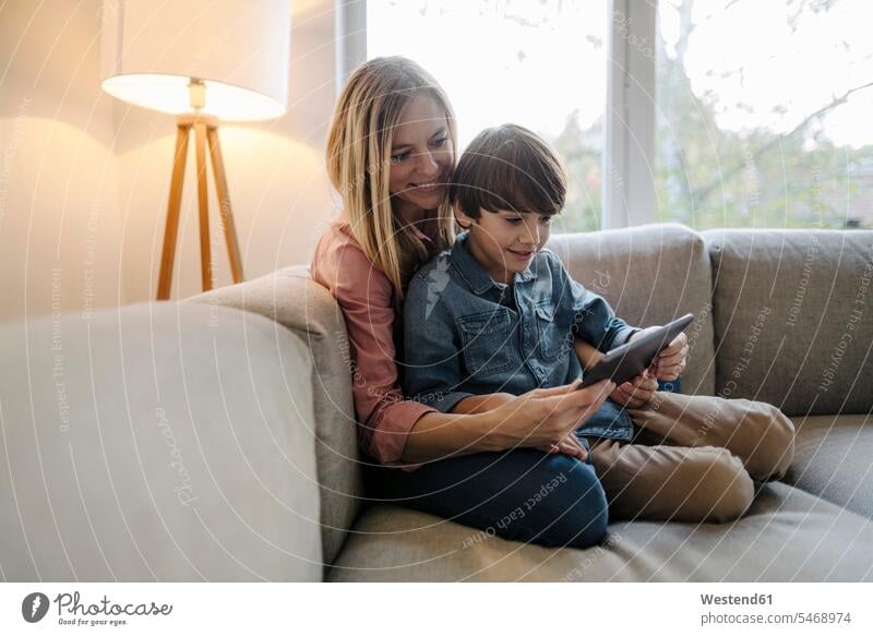 Mutter und Sohn sitzen auf dem Sofa und benutzen ein digitales Tablett Couch Couches Liege Sofas sitzend sitzt behüten behütet geborgen Sicherheit daheim