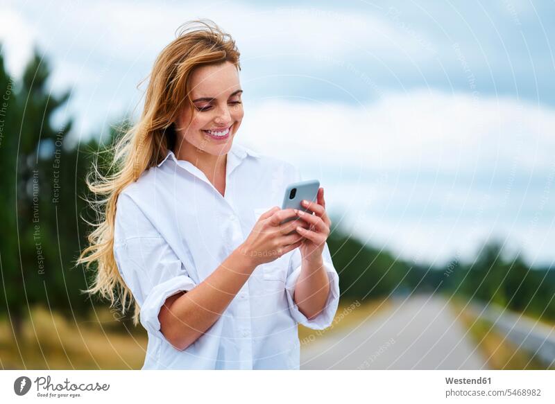 Glückliche Frau überprüft Handy auf Landstraße Touristen Telekommunikation telefonieren Handies Handys Mobiltelefon Mobiltelefone Lektüre sommerlich Sommerzeit