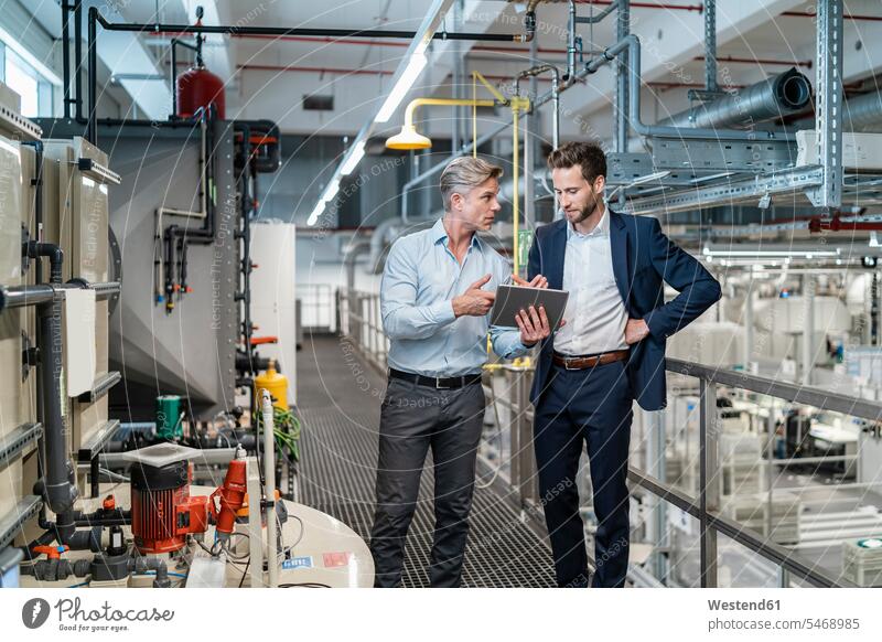 Zwei Geschäftsleute mit Tablette im Gespräch in einer modernen Fabrik Arbeitskollege Arbeitskollegen Kollege Partner Partnerschaften Job Berufe Berufstätigkeit