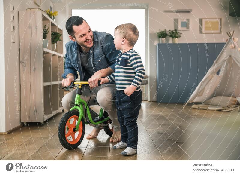 Vater hilft Sohn beim Fahren mit einem Balance-Fahrrad zu Hause Bikes Fahrräder Räder Rad lehren unterrichten beibringen fahren Kinderlaufrad Lauflernrad