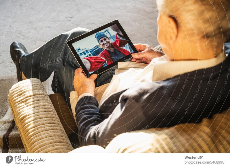 Großvater im Gespräch mit Enkelin per Videoanruf über digitales Tablet zu Hause Farbaufnahme Farbe Farbfoto Farbphoto Innenaufnahme Innenaufnahmen innen drinnen