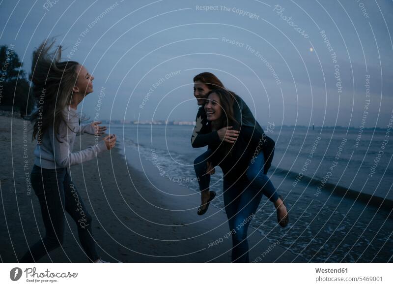 Deutschland, Hamburg, sorglose Mutter mit zwei Teenager-Mädchen am Strand am Elbufer bei Nacht nachts glücklich Glück glücklich sein glücklichsein Ufer