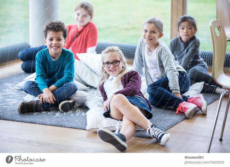 Porträt von lächelnden Schülern, die im Pausenraum der Schule auf dem Boden sitzen Schulen sitzend sitzt Portrait Porträts Portraits Böden Boeden Schulkind