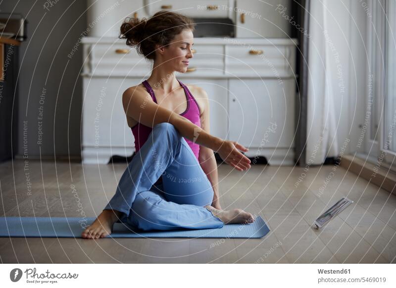 Frau schaut digitales Tablett an, während sie zu Hause Yoga praktiziert Farbaufnahme Farbe Farbfoto Farbphoto Innenaufnahme Innenaufnahmen innen drinnen Tag