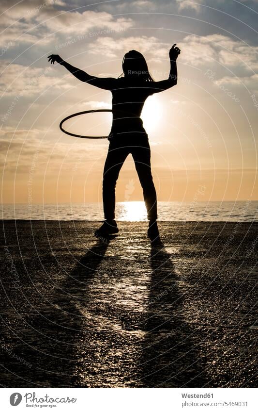 Glückliche Frau spielt mit Hula-Hoop-Reifen im Hafen bei Sonnenuntergang Contemporary Vorderansicht Frontalansicht von vorne frontal Außenaufnahme