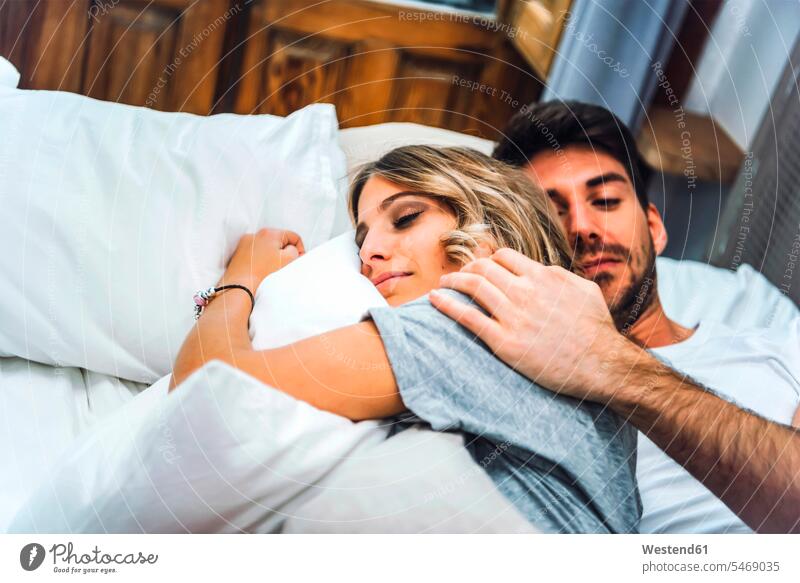 Zärtliches junges Paar liegt zu Hause im Bett Betten knuddeln schmusen schlafend Arm umlegen Umarmung Umarmungen freuen geniessen Genuss Glück glücklich sein