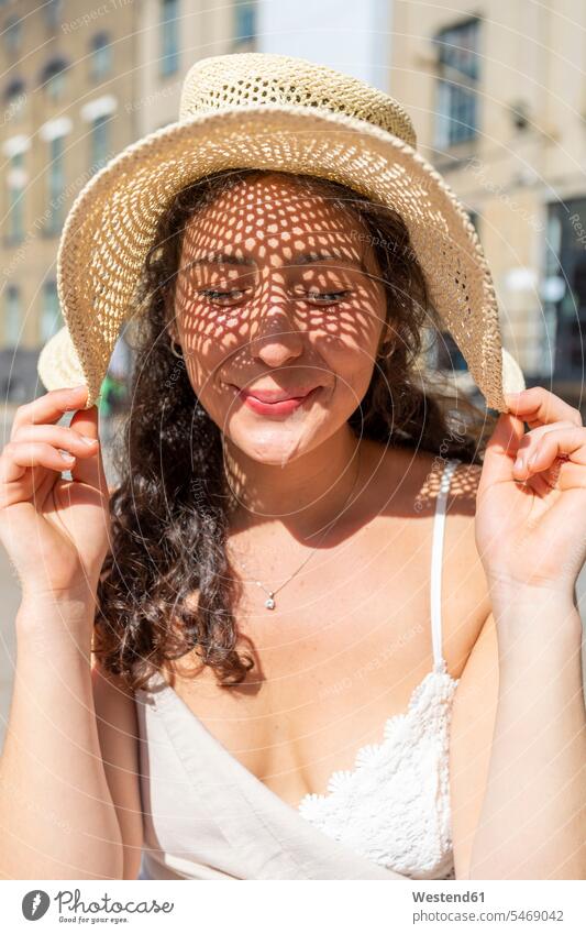 Nahaufnahme einer lächelnden schönen Frau mit geschlossenen Augen und Hut in der Stadt an einem sonnigen Tag Farbaufnahme Farbe Farbfoto Farbphoto