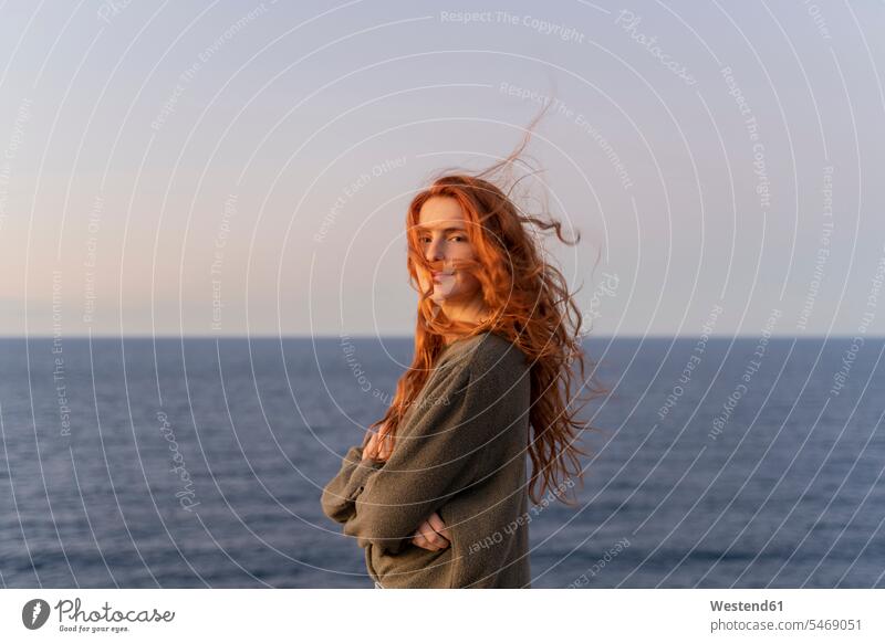 Porträt einer rothaarigen jungen Frau mit windgepeitschtem Haar an der Küste bei Sonnenuntergang, Ibiza, Spanien (value=0) Leute Menschen People Person Personen