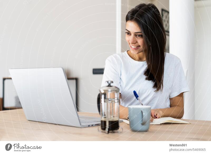 Junge Frau mit Laptop macht Notizen zu Hause Leute Menschen People Person Personen Europäisch Kaukasier kaukasisch 1 Ein ein Mensch eine nur eine Person single