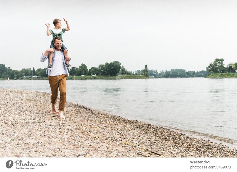 Glücklicher Vater trägt Sohn auf den Schultern am Flussufer Söhne tragen transportieren glücklich glücklich sein glücklichsein Fluesse Fluß Flüsse Papas Väter