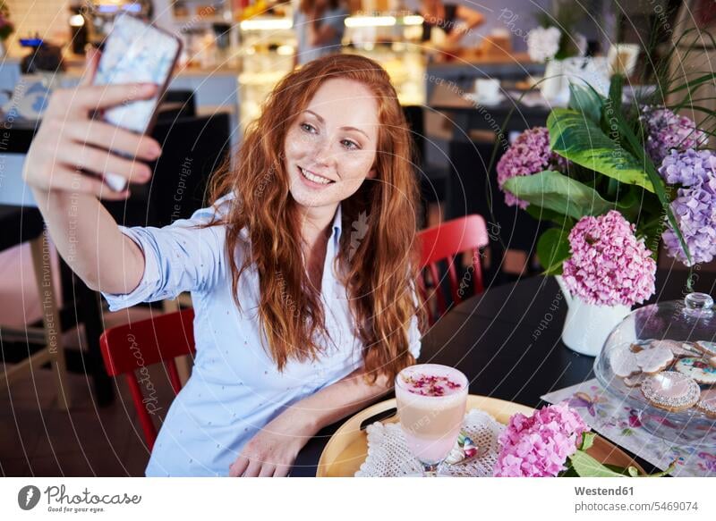 Lächelnde junge Frau macht ein Selfie in einem Café Handy Mobiltelefon Handies Handys Mobiltelefone Cafe Kaffeehaus Bistro Cafes Cafés Kaffeehäuser Selfies