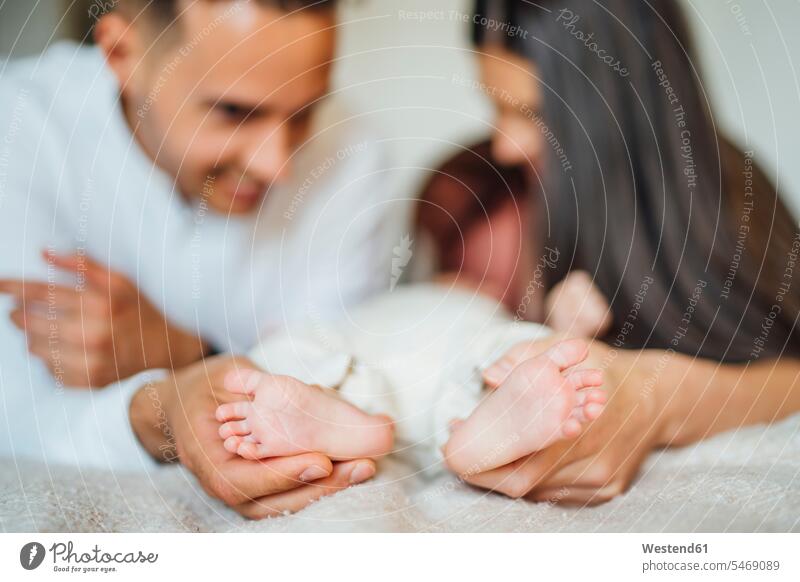 Eltern halten zu Hause die Füße des kleinen Jungen auf dem Bett Farbaufnahme Farbe Farbfoto Farbphoto Innenaufnahme Innenaufnahmen innen drinnen Tag
