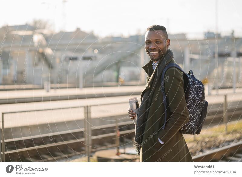 Porträt eines lächelnden Mannes mit wiederverwendbarem Becher, der auf den Zug wartet geschäftlich Geschäftsleben Geschäftswelt Geschäftsperson