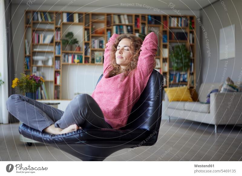 Mittlere erwachsene Frau mit Händen hinter dem Kopf, die sich zu Hause auf einem Stuhl entspannt Farbaufnahme Farbe Farbfoto Farbphoto Innenaufnahme