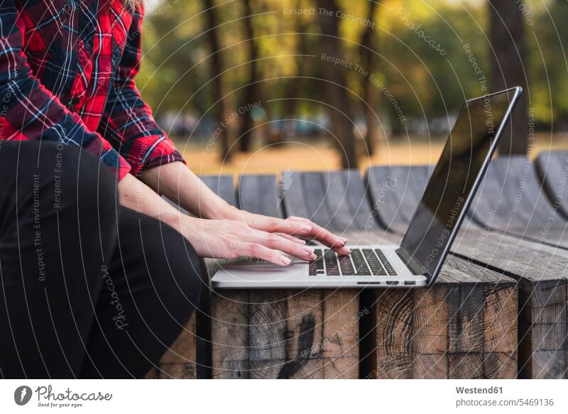 Junge Frau sitzt auf einer Bank im Freien und arbeitet an einem Laptop, Teilansicht Sitzbänke Bänke Sitzbank weiblich Frauen sitzen sitzend arbeiten Arbeit