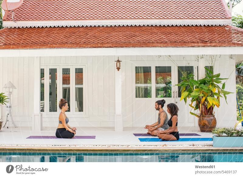 Zwei Frauen und ein Mann praktizieren Yoga am Pool Beckenrand Swimmingpool Swimmingpools Schwimmbecken Swimming Pool Swimming Pools üben ausüben Übung
