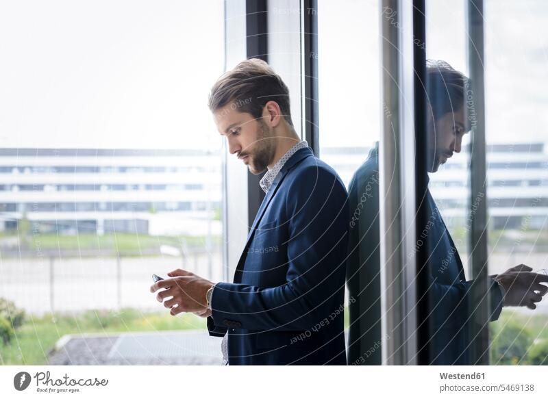 Junger Geschäftsmann mit Smartphone am Fenster Leute Menschen People Person Personen Europäisch Kaukasier kaukasisch 1 Ein ein Mensch eine nur eine Person