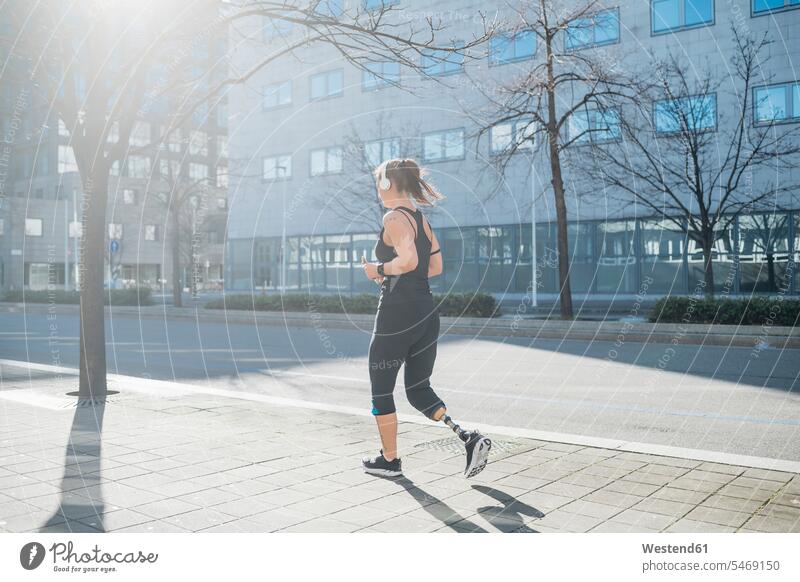 Sportliche junge Frau mit Beinprothese läuft in der Stadt Kopfhoerer hoeren rennen Farben Farbtoene Farbton Farbtöne schwarze schwarzen schwarzer schwarzes fit
