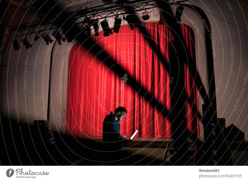 Regisseur steht vor der Bühne im Theater und benutzt einen Laptop Mann Männer männlich Bühnen Zuschauerraum Theaterregisseur stehen stehend benutzen benützen