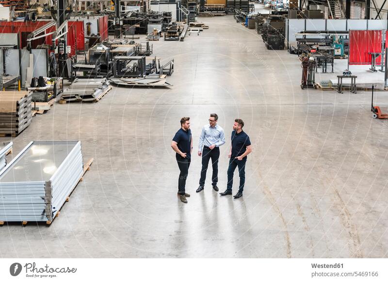 Drei Männer stehen und reden in der Fabrikhalle Kollegen Arbeitskollegen Produktionshalle Montagehalle Fabriken stehend steht Mann männlich sprechen Erwachsener