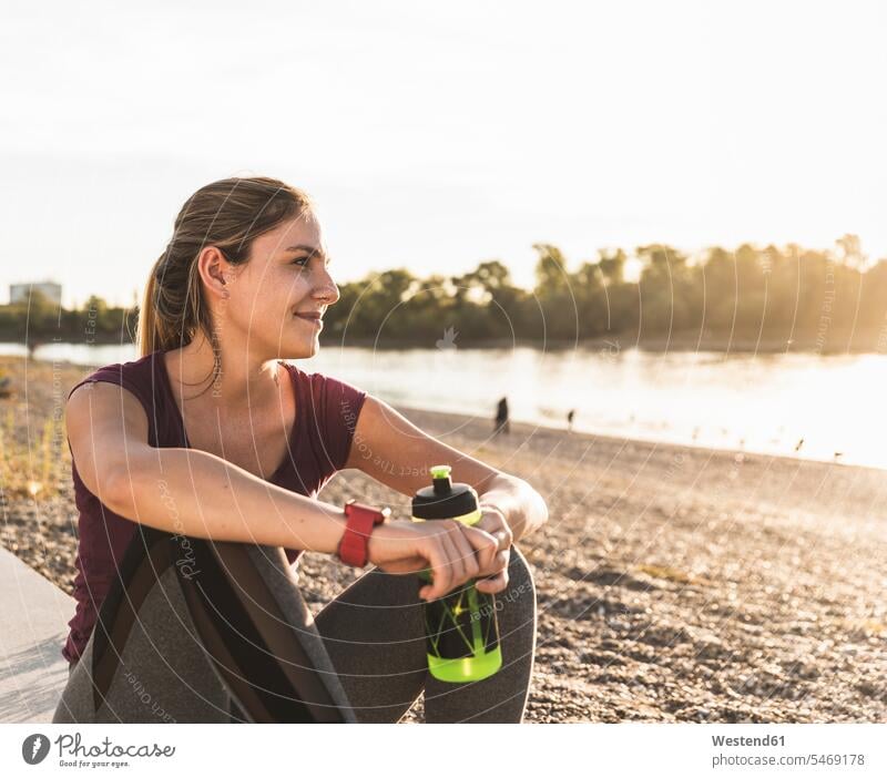 Junge Frau nimmt eine Pause nach dem Training am Fluss Fluesse Fluß Flüsse erholen erholend Erfrischung erfrischen erfrischend sitzen sitzend sitzt trainieren