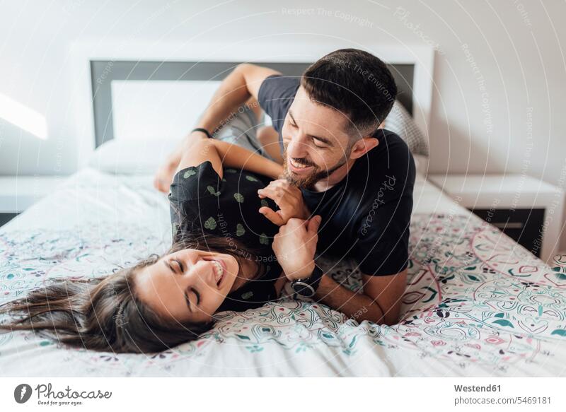 Lächelndes Paar spielt zu Hause auf dem Bett im Schlafzimmer Farbaufnahme Farbe Farbfoto Farbphoto Innenaufnahme Innenaufnahmen innen drinnen Tag