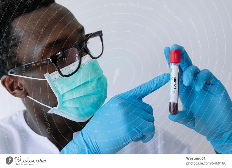 Nahaufnahme eines Afro-Arztes mit Coronavirus-Blutprobe vor weissem Hintergrund Farbaufnahme Farbe Farbfoto Farbphoto Spanien weißer Hintergrund