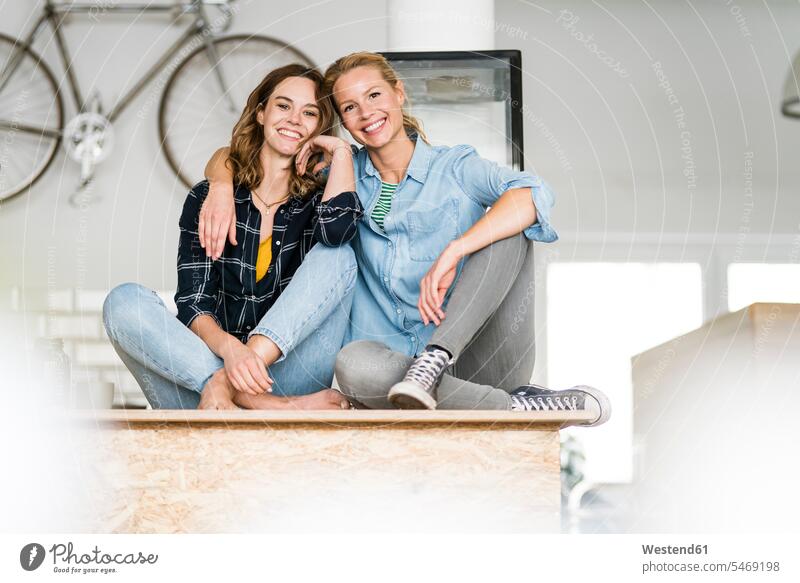 Zwei junge Frauen sitzen im Schneidersitz auf der Theke ihres Coffeeshops, mit ausgebreiteten Armen Leute Menschen People Person Personen Europäisch Kaukasier