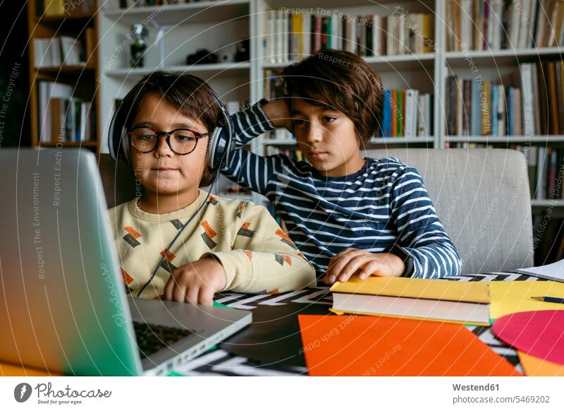 Junge schaut mit der Hand im Haar auf den Laptop, während er mit einem männlichen Freund im Wohnzimmer Hausunterricht hat Farbaufnahme Farbe Farbfoto Farbphoto