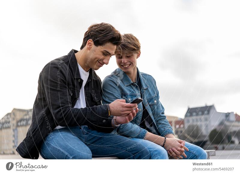 Dänemark, Kopenhagen, zwei junge Männer sitzen auf einer Bank und benutzen ein Mobiltelefon Kobenhavn Reisende Reisender ausruhen Rast Erholung erholen SMS