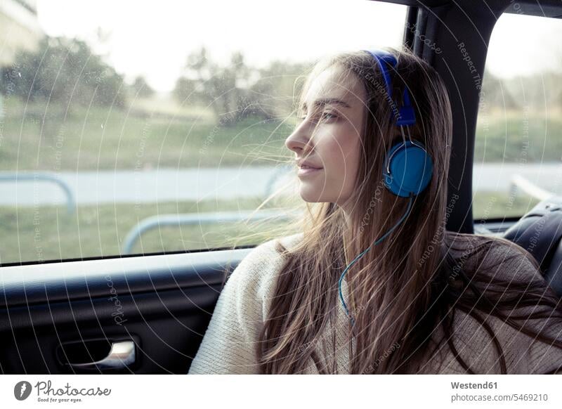 Junge Frau mit vom Wind zerzausten Haaren in einem Auto und Kopfhörern weiblich Frauen Wagen PKWs Automobil Autos Kopfhoerer Windstoß windig Erwachsener
