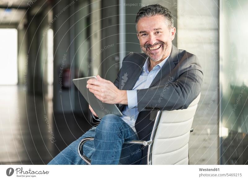 Porträt eines glücklichen reifen Geschäftsmannes mit Tablett auf einem Stuhl im Büro sitzend Job Berufe Berufstätigkeit Beschäftigung Jobs geschäftlich