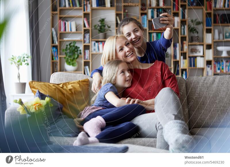 Mutter und ihre Töchter sitzen auf der Couch und machen Smartphone-Selfies sitzend sitzt Sofa Couches Liege Sofas Tochter Mami Mutti Mütter Mama fotografieren
