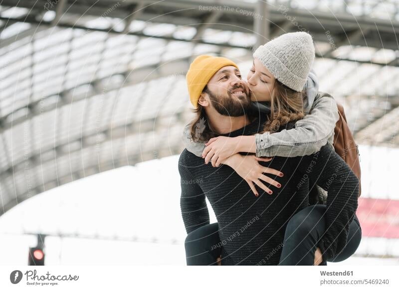 Glückliches junges Paar mit Spaß und Küssen auf dem Bahnsteig, Berlin, Deutschland Touristen Rucksäcke Kuss verreisen Arm umlegen Umarmung Umarmungen