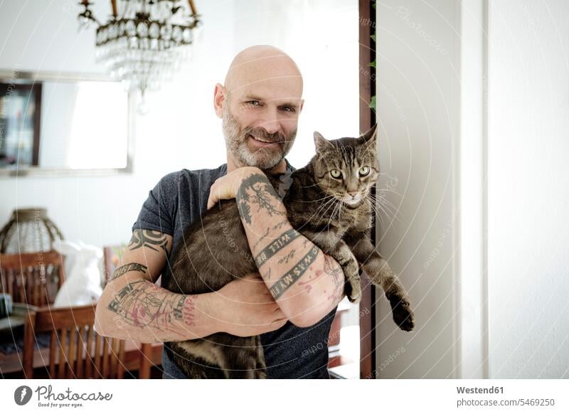 Tätowierter Mann trägt seine Katze halten Katzen tätowiert Zuhause zu Hause daheim Haustier Haustiere Tier Tierwelt Tiere Tattoo Tätowierungen Tatoos