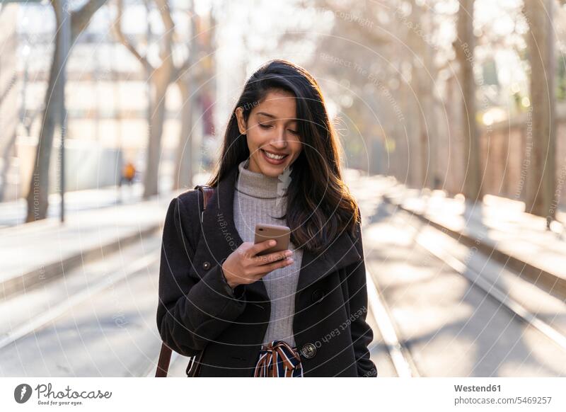 Lächelnde junge Frau mit Smartphone auf Straßenbahnlinie Informationen Transport Transportwesen Bahnen Straßenbahnen Tram Trambahn Telekommunikation