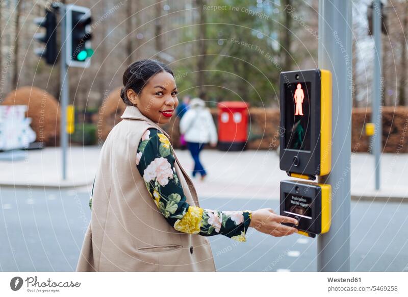 UK, London, Porträt einer lächelnden Frau, die den Knopf einer Fußgängerampel drückt drücken weiblich Frauen Portrait Porträts Portraits Fußgängerampeln