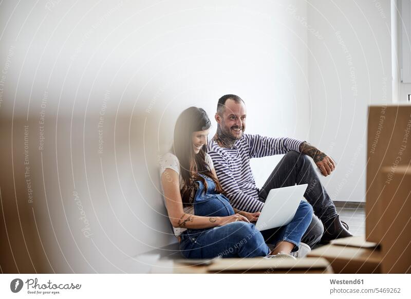 Glückliches Paar arbeitet am Laptop, während es im häuslichen Zimmer sitzt Farbaufnahme Farbe Farbfoto Farbphoto Innenaufnahme Innenaufnahmen innen drinnen Tag