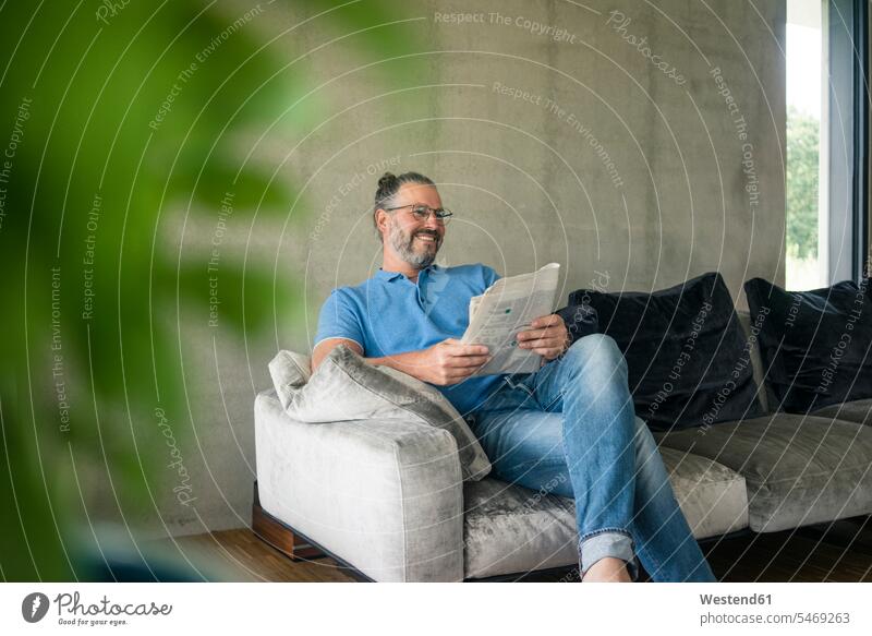 Lächelnd reifen Mann sitzt auf Couch zu Hause lesen Zeitung Leute Menschen People Person Personen Europäisch Kaukasier kaukasisch 1 Ein ein Mensch eine