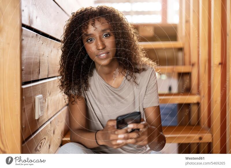 Junge Frau benutzt Mobiltelefon, während sie zu Hause auf einer Treppe sitzt Farbaufnahme Farbe Farbfoto Farbphoto Innenaufnahme Innenaufnahmen innen drinnen