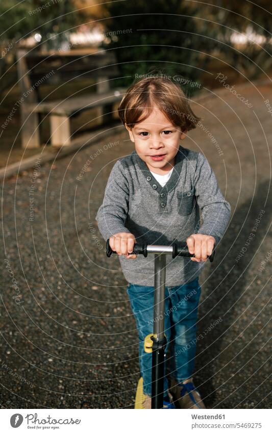 Porträt eines kleinen Jungen mit Roller Kinderfahrzeuge Tretroller stehend steht Parkanlage Parkanlagen Parks außen draußen im Freien frontal Frontalansicht