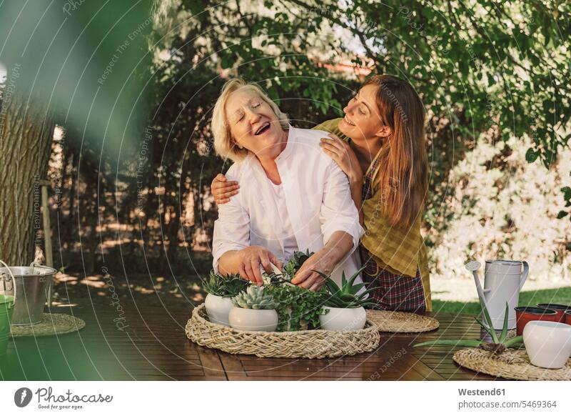 Tochter sieht fröhliche Mutter an, die sich um die Pflanzen auf dem Tisch im Hof kümmert Farbaufnahme Farbe Farbfoto Farbphoto Spanien Freizeitbeschäftigung