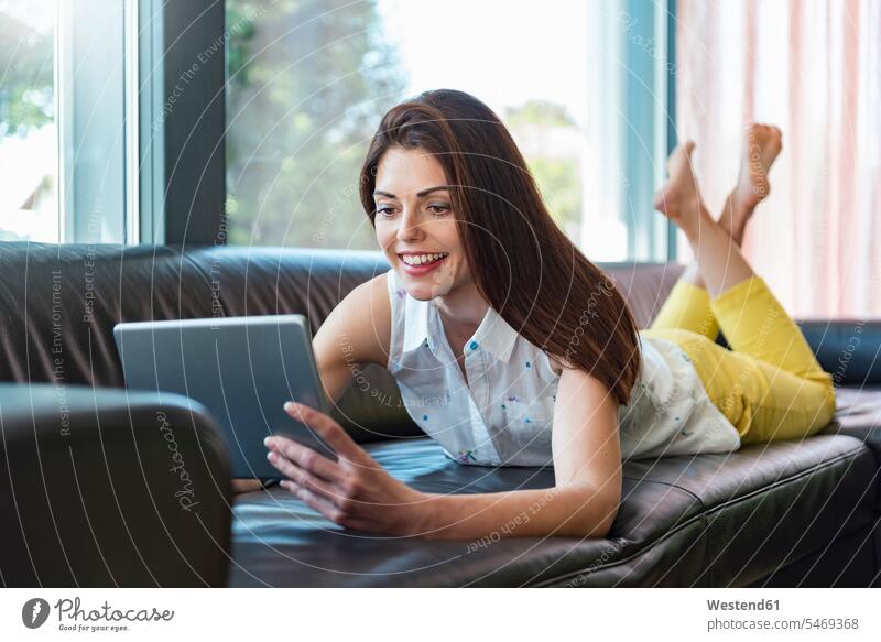 Lächelnde Frau liegt zu Hause auf dem Sofa und benutzt eine Tablette Couches Liege Sofas liegen liegend weiblich Frauen lächeln Tablet Computer Tablet-PC