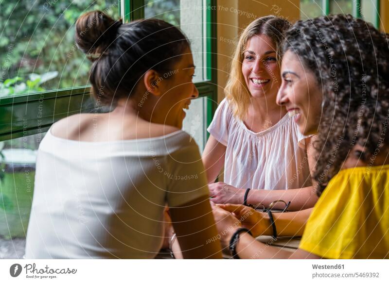 Drei glückliche junge Frauen treffen sich in einem Cafe Leute Menschen People Person Personen Europäisch Kaukasier kaukasisch Asiaten Asiatisch asiatische
