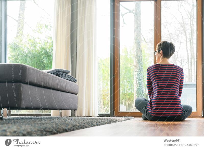 Rückenansicht einer Frau, die auf dem Boden des Wohnzimmers sitzt und aus dem Fenster schaut Fußboden Fußboeden Fussboeden Fussboden Fußböden Fussböden weiblich